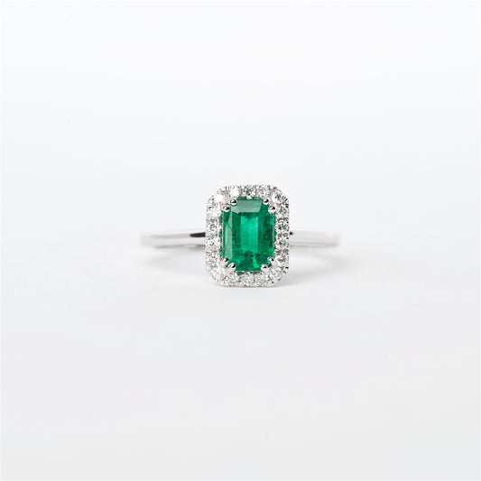 An 18K white gold emerald and diamond ring with a .77 CT very fine emerald cut Colombian emerald surrounded by a halo of round brilliant diamonds.