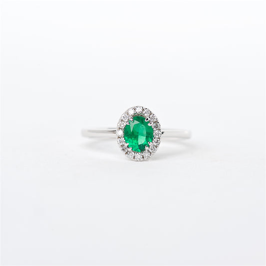 An 18K white gold ring featuring a vibrant green Colombian emerald centerpiece surrounded by round brilliant diamonds.