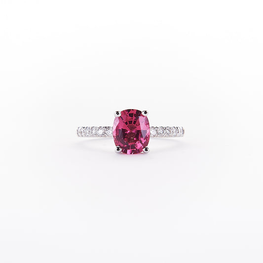 An 18K white gold ring with a rare red spinel centerpiece and round brilliant diamond halo, set on a white band.